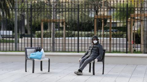 امرأة تجلس وحيدة مرتدية كمامة في حديقة عامة خالية من الناس في مدينة نيس الفرنسية